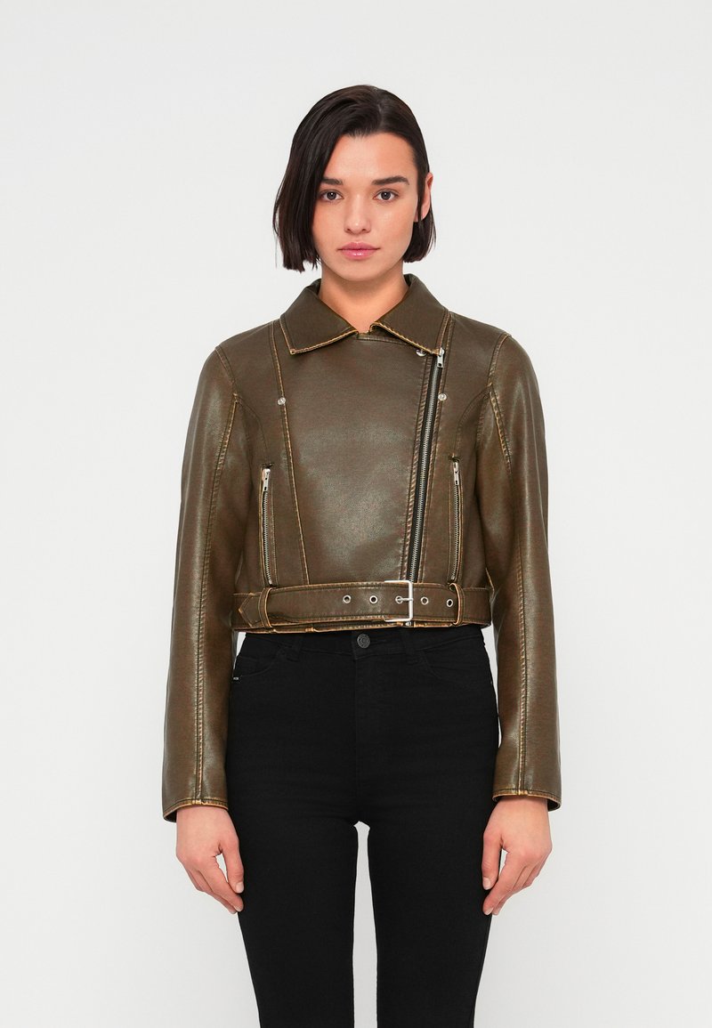 Κοντό δερμάτινο μπουφάν ελιάς πράσινου χρώματος με γιακά, κλείσιμο με φερμουάρ και δύο μπροστινές θήκες με φερμουάρ. Διαθέτει κίτρινο ραφές σε αντίθεση.