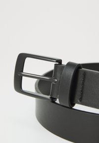 Ceinture en cuir noir avec une boucle rectangulaire noire mate et une finition lisse. La ceinture mesure environ 3 cm de large.