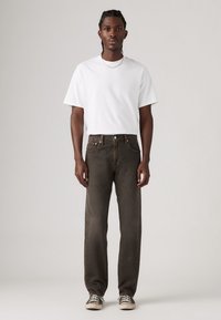 Camiseta blanca de manga corta combinada con jeans rectos de color gris oscuro y zapatillas en blanco y negro. Diseño sencillo con un corte relajado.