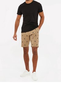 Schwarzes Rundhals-T-Shirt, beige Shorts mit Tukan-Muster, flache Vorderseite, seitliche Taschen, kombiniert mit weißen Sneakers.