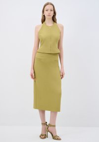 Top s halter výstřihem a zipem vpředu v olivové zelené barvě, spárovaný s odpovídající tužkovou sukní. Oba kousky mají elegantní linie a minimální detaily. Celý vzhled dotvářejí sandály na vysokém podpatku.