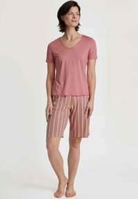 Een lichtroze t-shirt met korte mouwen en een v-hals, gecombineerd met gestreepte shorts in roze, wit en beige. Zachte stof, shorts tot de knie.