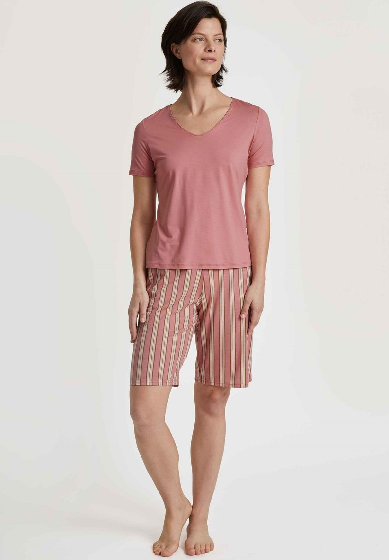 Een lichtroze t-shirt met korte mouwen en een v-hals, gecombineerd met gestreepte shorts in roze, wit en beige. Zachte stof, shorts tot de knie.