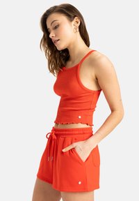 Röd ribbad tanktop med vågiga kanter och matchande röda shorts med elastisk midja och sidofickor. Tillverkad av mjukt, lätt tyg.
