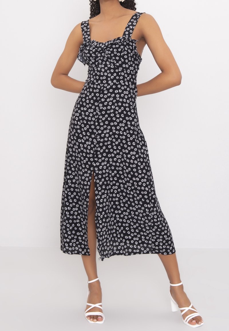 Černé květinové šaty s bílými vzory sedmikrásek, zúžený korzet, silné ramínka a rozparek až ke stehnům. Vyrobeno z lehké tkaniny.