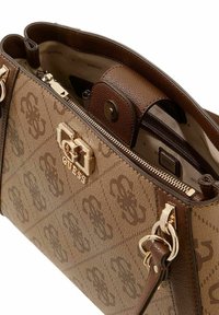 Sac à main en toile marron avec motif monogramme, ferrures dorées et double poignées. Fermeture éclair dévoilant un intérieur beige avec détails de la marque.