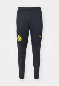 Zwarte sportbroek gemaakt van lichtgewicht stof, met een geel Borussia Dortmund-logo, Puma-branding en ritsen aan de onderkant.