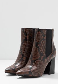 Bottes cheville imprimées serpent marron et noir avec bouts pointus, talons blocs hauts et panneaux latéraux élastiques ; surface texturée brillante.