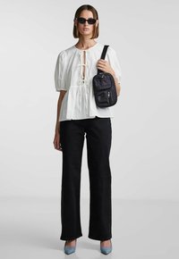 Hvit bluse med puffermer og frontknuter, svarte høyhårede jeans og svart crossover-veske; blå spisse hæler fullfører antrekket.