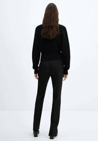 Pull en maille noire à manches longues et à la silhouette légèrement raccourcie, associé à un pantalon noir ajusté et des bottes à talons épais.