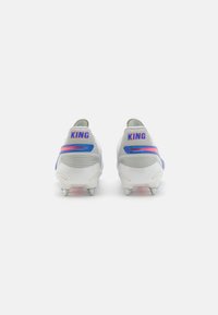 Botas de fútbol en gris y blanco con acentos en azul y rosa. Presentan un upper texturizado y tachuelas metálicas para un mejor agarre. "KING" escrito en el talón.