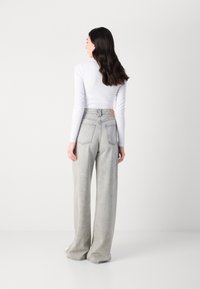 Lys grå vide jeans med høy midje, med baklommene og et lite merkenavn nær linningen. Teksturert denim-materiale.