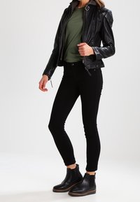 Czarna skórzana kurtka z akcentami na ramionach, oliwkowa koszulka, czarne obcisłe dżinsy i czarne botki za kostkę z brązowymi podeszwami.