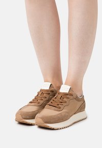 Brown sneakers made of suede and leather with a textured finish, featuring lace-up closure and white rubber sole. Logo on heel tab.