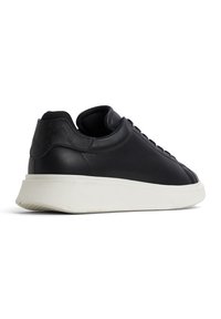 Černé kožené tenisky s hladkým povrchem, zakulacenou špičkou, polstrovaným límcem a bílou texturovanou gumovou podrážkou. Jednoduchý design na šněrování.