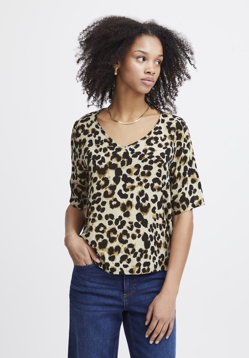 Kortærmet T-shirt i leopardmønster i beige og sort med V-udskæring; let stof og afslappet pasform. Båret med blå jeans.