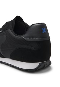 Basket noire en tissu texturé avec des détails en daim, semelle blanche et une petite étoile bleue sur la languette du talon.