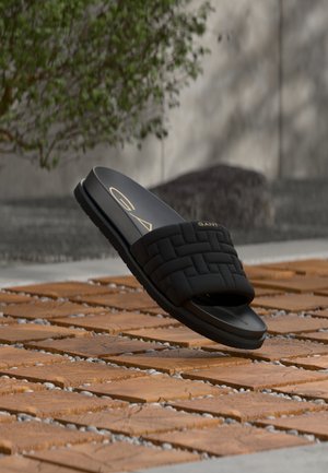 Μαύρο πλεκτό σανδάλι σλάιντ με επίπεδη ελαστική σόλα, με λείο φινίρισμα και χρυσό λογότυπο στο πάνω λουράκι. Ελαφρύ σχέδιο.