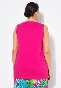 Top fucsia senza maniche realizzato in un tessuto liscio, con scollo rotondo e taglio dritto, indossato con pantaloni floreali a fantasia.