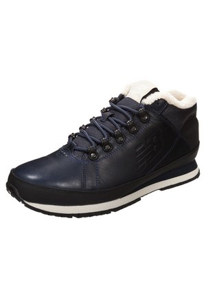 Navy blue leather hiking shoe with white fleece lining, metal eyelets, and black rubber outsole; features textured surface and logo detail.