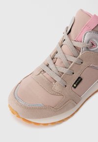 Hellbraune und rosa Gore-Tex Sneaker mit beigen Schnürsenkeln, Wildleder- und Stoffeinsätzen, reflektierenden Details und einer Gummisohle, schräg auf weißem Hintergrund.