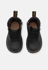 Botas de cuero negras hasta el tobillo con punta redonda, suela gruesa, costuras amarillas, ojales de metal y cordones negros. Incluye una lengüeta en el talón.