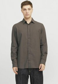 Camisa de manga larga marrón, abotonada, en una tela ligera con cuello, botones frontales y un corte relajado, combinada con pantalones vaqueros oscuros.