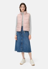 Light pink puffer vest with high collar, paired with a gray turtleneck and a denim knee-length skirt featuring front buttons. White sneakers.