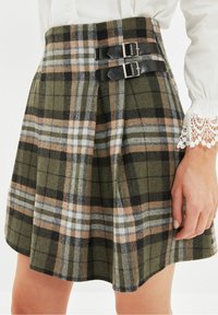 Vihreä ruudullinen hame, joka on valmistettu villasekoitteesta. Hameessa on liesituuletinmuotoilu, kaksi mustasta nahasta valmistettua solkea sekä kontrastoivia valkoisia, mustia ja persikkavärisiä kuvioita.