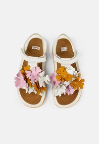 Valkoiset nahka-sandalsit, joissa on värikkäitä kukka-applikaatioita vaaleanpunaisena, oranssina ja valkoisena, sekä Velcro-nauha ja ruskea teksturoidun pohjan.