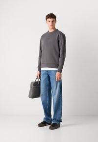 Gray sweatshirt with a round neckline, paired with loose-fitting blue denim jeans. The model holds a gray leather bag with a smooth texture.