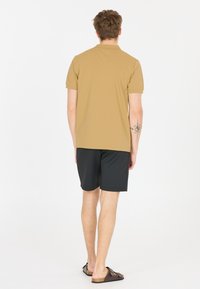 Ljusbrun pikétröja med klassisk krage, kombinerad med svarta shorts och bruna sandaler. Slät textur, korta ärmar, enkelt mönster.