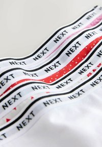 Elastieken in wit, rood en roze met zwarte "NEXT" tekst, met patronen van stippen en driehoeken, gerangschikt in lagen.