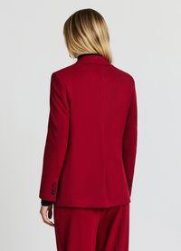 Blazer rosso con taglio sartoriale, chiusura con un solo bottone e dettagli del colletto in nero. Tessuto liscio e taglio elegante, con dettagli a bottoni sulle maniche.