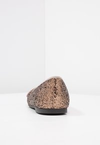 Bailarinas de bronce con purpurina, con puntera redondeada y suela negra. Superficie texturizada con un acabado brillante, que presenta un borde superior liso.