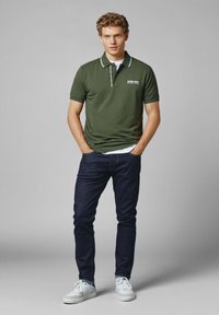 Mörkgrön pikétröja med vit krage, korta ärmar och logodetalj, tillsammans med mörka jeans och vita sneakers. Avslappnad passform.