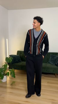 Black cardigan with vertical stripes in brown, white, and orange, paired with black pants and black shoes. Simple design, textured fabric.