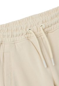 Beige Baumwoll-Sweatpants mit elastischem Bund, Kordelzug und seitlichen Taschen. Glatte Textur mit einer lockeren Passform.