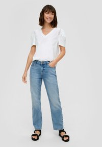 Witte V-hals t-shirt met puffmouwen met kantdetails, gecombineerd met lichtblauwe rechte jeans en zwarte platform sandalen.