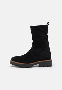 Bota de ante negra con un eje arrugado, punta redonda y una suela de goma resistente con un diseño de tacos pronunciados y un detalle de costura en contraste.