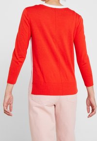 Czerwony dziany sweter z okrągłym dekoltem i rękawami do łokcia, z bocznymi rozcięciami i kontrastującym wzorem z tyłu.