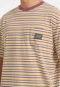 Gestreiftes T-Shirt mit kurzen Ärmeln in Gelb, Burgunder und Marineblau. Verfügt über einen Rundhalsausschnitt und eine linke Brusttasche mit einem Etikett-Label. Aus weichem Baumwollmaterial.