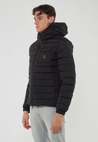 Giacca nera imbottita con chiusura a zip, polsini elastici, cappuccio e tasca sul petto con una piccola etichetta logo. Texture liscia e leggera.