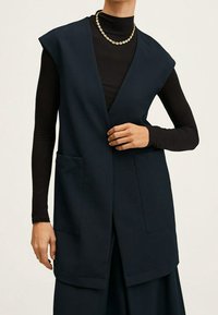 Chaleco sin mangas azul marino con cuello en V profundo, hecho de tela lisa, con dos bolsillos frontales y un diseño suelto y estructurado.