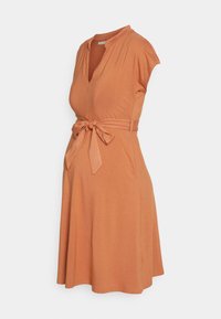 Vestido de maternidade em laranja queimado, com decote em V, mangas curtas e um laço de tecido na cintura. Feito de material macio e elástico.