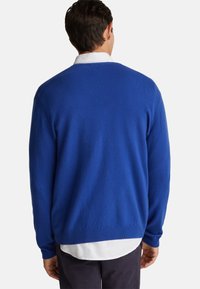 Königsblauer Pullover mit weicher Textur, gerippten Bündchen und Saum. Über einem weißen Hemd getragen, das ein klassisches Rundhalsausschnitt-Design präsentiert.