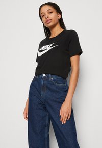 Zwarte korte mouwen T-shirt met een groot wit Nike-logo, gecombineerd met high-waisted donkerblauwe denim jeans met een relaxte pasvorm en een klassiek ontwerp.