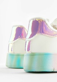 Scarpe da ginnastica bianche con accenti iridescenti sul tallone, caratterizzate da una texture liscia e una suola traslucida di un blu chiaro.