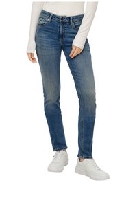 Denim jeans in medium blue with a slim fit, featuring a classic five-pocket design and subtle fading. Paired with white sneakers.