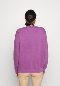 Fialový crewneck svetr vyrobený z měkké bavlněné směsi, s volným střihem, žebrovanými manžetami a lemem. Minimalistický design, zobrazený ze zadní strany.